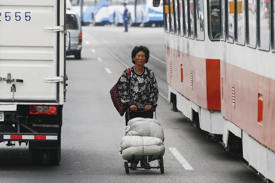 Βόρεια Κορέα - Επέτειος 70 χρόνων από την ίδρυση του Εργατικού Κόμματος Κορέας. Μια γυναίκα σέρνει το καρότσι της ανάμεσα σε οχήματα στο κέντρο της Πιονγιάνγκ.