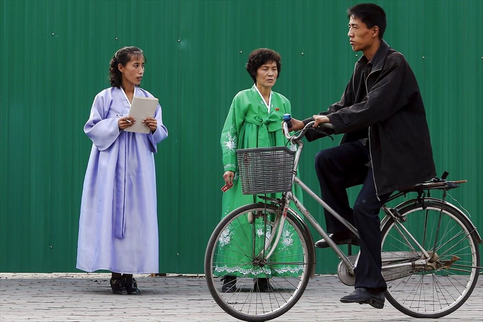 Βόρεια Κορέα - Επέτειος 70 χρόνων από την ίδρυση του Εργατικού Κόμματος Κορέας. Ένας άντρας περνά με το ποδήλατό του μπροστά από γυναίκες με παραδοσιακές φορεσιές στο κέντρο της Πιονγιάνγκ.