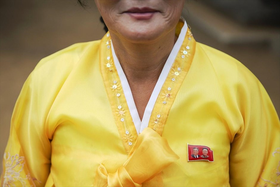 Βόρεια Κορέα - Επέτειος 70 χρόνων από την ίδρυση του Εργατικού Κόμματος Κορέας. Μια γυναίκα με παραδοσιακή στολή φορά καρφίτσα με τα πρόσωπα του ιδρυτή της Β. Κορέας Κιμ Ιλ Σουνγκ (αριστερά) και του πρώην ηγέτη Κιμ Γιονγκ Ιλ, καθώς υποδέχεται ξένους δημοσιογράφους σε ναό έξω από την Πιονγιάνγκ, κατά τη διάρκεια ξενάγησης που έχει οργανωθεί από την κυβέρνηση. 