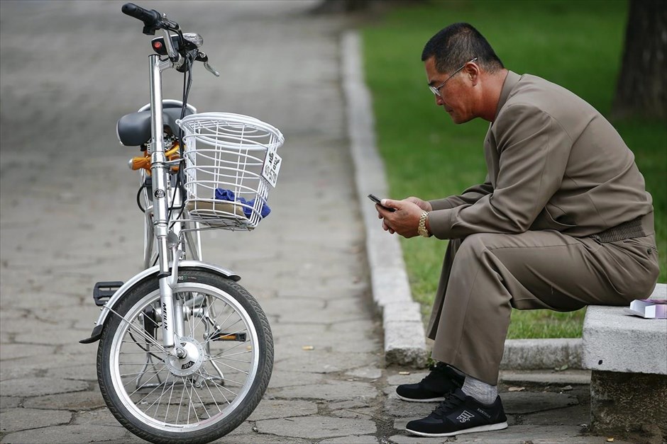 Βόρεια Κορέα - Επέτειος 70 χρόνων από την ίδρυση του Εργατικού Κόμματος Κορέας. Ένας άντρας χρησιμοποιεί το κινητό του, ενώ έχει στηρίξει δίπλα του το ηλεκτρικό του ποδήλατο.