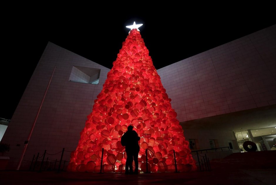 Χριστούγεννα στον κόσμο. Ζευγάρι αγκαλιάζεται μπροστά από δέντρο φτιαγμένο από πλαστικά καλάθια, έξω από το Μουσείο Ιστορίας του Μοντερέι, στο Μεξικό.