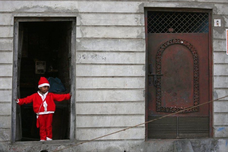 Εκδήλωση για τα μη προνομιούχα παιδιά στην Ινδία. Ένα παιδάκι ντυμένο με στολή του Αγίου Βασίλη στέκεται στην πόρτα ενός κτηρίου, όπου διοργανώνεται εκδήλωση της πρωτοβουλίας για βιώσιμη εκπαίδευση των μη προνομιούχων παιδιών, στην ινδική πόλη Αμριτσάρ. Την εν λόγω καμπάνια υλοποιεί μη κυβερνητική οργάνωση με στόχο την παροχή εκπαίδευσης των παιδιών που ζουν στις παραγκουπόλεις της ασιατικής χώρας.&nbsp;