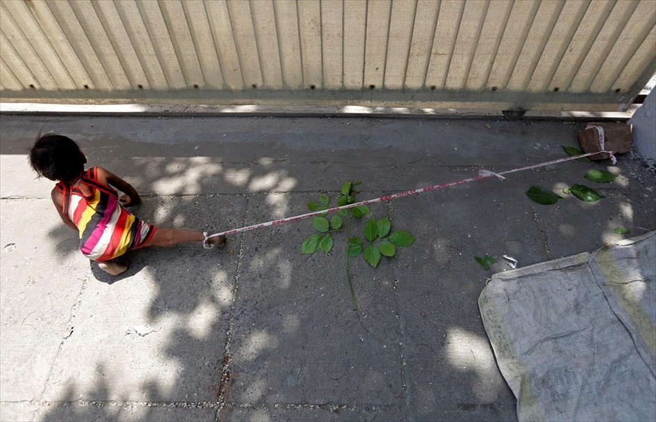 Ανασκόπηση 2016: Ο λόγος στους φωτογράφους . Η ηλικίας 15 μηνών Σιβάνι είναι δεμένη με σχοινί από τον αστράγαλο, ενώ οι γονείς της εργάζονται, στο Αχμενταμπάντ της Ινδίας (19 Απριλίου 2016).Ο φωτογράφος Αμίτ Ντέιβ αφηγείται:Έβγαζα φωτογραφίες από την καθημερινότητα στο Αχμενταμπάντ, όταν είδα μερικούς εργάτες να τραβούν βαριά ηλεκτρικά καλώδια και αισθάνθηκα ότι θα δημιουργούνταν ένα ωραίο κάδρο. Το φως δεν ήταν τόσο καλό κι έτσι περίμενα να βελτιωθεί. Τα παιδιά των εργατών έτρεχαν τριγύρω κι έπαιζαν στην άκρη του δρόμου, αλλά ένα παιδί καθόταν μόνο του και πλησίασα να δω για ποιο λόγο.Η ηλικίας 15 μηνών Σιβάνι τραβούσε την πλαστική ταινία με την οποία είχε δέσει το πόδι της η μητέρα της. Η ταινία ήταν πιασμένη σε έναν βράχο στο εργοτάξιο. Ξυπόλητη και καλυμμένη από σκόνη και υπό θερμοκρασία 40 βαθμών Κελσίου, πέρασε 9 ώρες δεμένη με την κορδέλα που έγραφε τη λέξη «προσοχή».Η μητέρα του κοριτσιού, Σάρτα Καλάρα, υποστηρίζει ότι δεν έχει άλλη επιλογή για να φυλάξει την κόρη της, όση ώρα αυτή και ο σύζυγός της εργάζονται σε εκσκαφές του εδάφους για την τοποθέτηση καλωδίων, κερδίζοντας 3,8 δολάρια την ημέρα ο καθένας.«Την δένω για να μη βγει στον δρόμο. Ο μικρός μου γιος είναι 3,5 χρονών και δεν μπορεί να τη φροντίσει», λέει η 23χρονη. «Αυτή η περιοχή έχει κίνηση. Δεν έχω άλλη επιλογή. Το κάνω για την ασφάλειά της».Όπως λένε οι γονείς, τα παιδιά μένουν μαζί τους μέχρι τα 7-8 τους χρόνια, οπότε πηγαίνουν να ζήσουν με τους παππούδες τους. Η Καλάρα υποστηρίζει ότι οι εργοδότες δεν ασχολήθηκαν με το πρόβλημά της. «Δεν τους ενδιαφέρουμε εμείς ή τα παιδιά μας, το μόνο που τους απασχολεί είναι η δουλειά τους», καταλήγει.