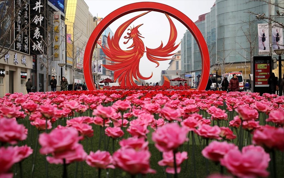 Προετοιμασίες για την κινεζική πρωτοχρονιά . Κόσμος περπατά δίπλα σε πλαστικά λουλούδια και έναν μεγάλο διακοσμητικό κόκορα που έχουν στηθεί για τον εορτασμό του επερχόμενου σεληνιακού νέου έτους στο Πεκίνο. Το κινεζικό σεληνιακό νέο έτος, γνωστό και ως Εαρινό φεστιβάλ, θα εορταστεί στις 28 Ιανουαρίου, την πρώτη ημέρα του «έτους του κόκορα».