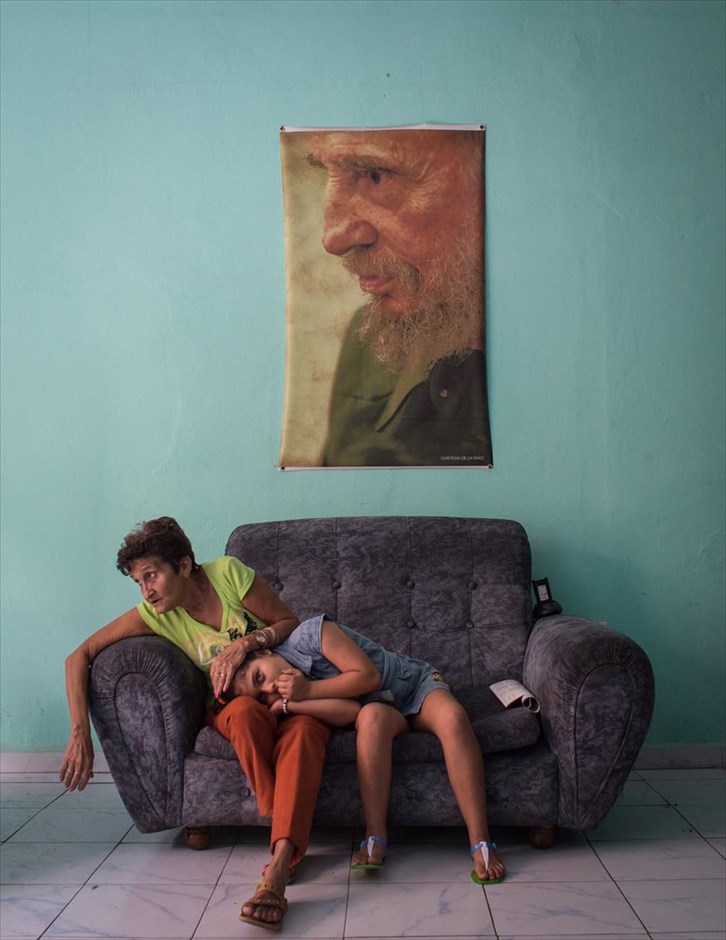 World Press Photo - People/Singles -3. Η Ρωσίδα φωτογράφος Kristina Kormilitsyna της εφημερίδας Kommersant κέρδισε το τρίτο βραβείο στην κατηγορία «People, Singles». Στη φωτογραφία, μία γυναίκα χαϊδεύει το κεφάλι ενός κοριτσιού, ενώ αυτό ξεκουράζεται στην αγκαλιά της, καθώς περιμένουν καθισμένες στον καναπέ ενός αστυνομικού τμήματος στην Καμαγουέι της Κούβας, με ένα πορτραίτο του Φιντέλ Κάστρο να κρέμεται από πάνω τους.