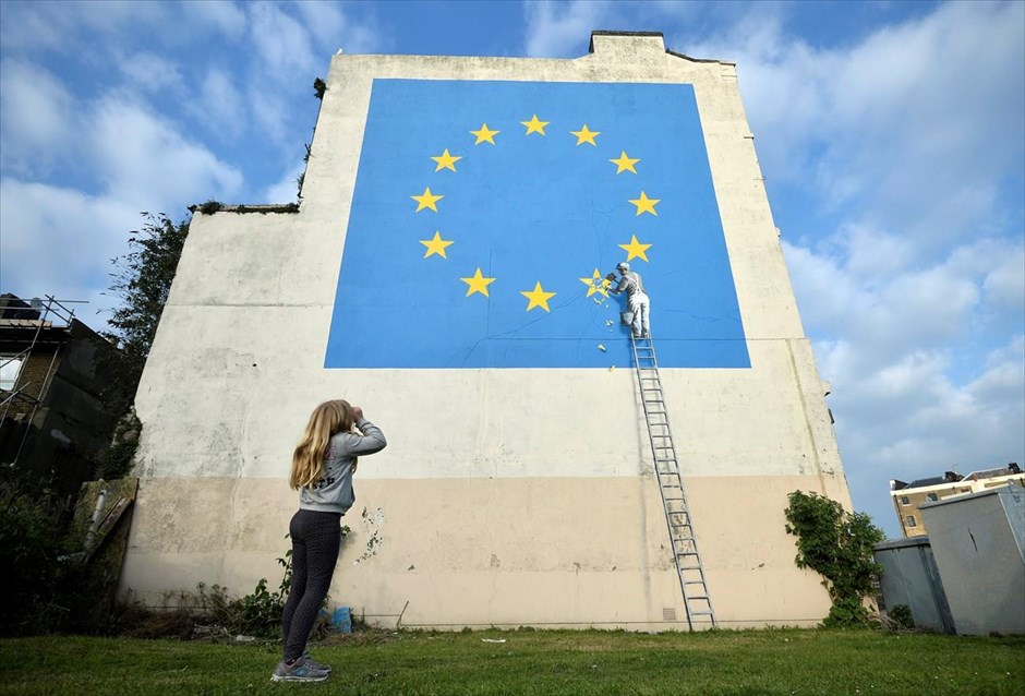 Ο Bansky «χτυπά» στο Ντόβερ με έργο αφιερωμένο στο Brexit. Μια έκπληξη περίμενε το πρωί της Κυριακής τους κατοίκους Ντόβερ, στη νοτιοανατολική Αγγλία, με τον γνωστό δημιουργό γκράφιτι Banksy να σχεδιάζει τη νύχτα ένα έργο αφιερωμένο στο Brexit, σε τοίχο κτηρίου της πόλης. Το γκράφιτι απεικονίζει έναν εργάτη να απομακρύνει από τη σημαία της Ευρωπαϊκής Ένωσης ένα από τα 12 αστέρια. Αν και για κάποιες ώρες δεν είχε γίνει γνωστό ποιος κρυβόταν πίσω από την τοιχογραφία, ο Banksy αποκάλυψε το απόγευμα της Κυριακής ότι σχεδίασε το συγκεκριμένο έργο, δημοσιεύοντας σχετικές φωτογραφίες στη σελίδα του στο Instagram.