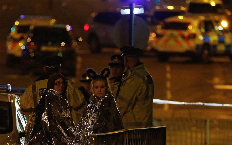 Two women wrapped in thermal blankets look on near the Manchester Arena. 