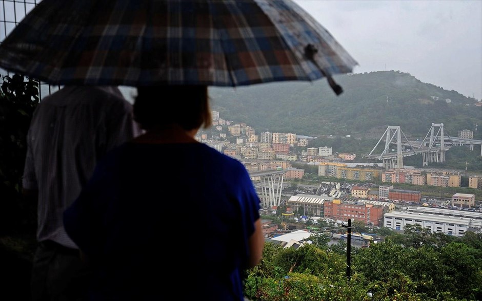 Θέα στην... καταστροφή. Ένα ζευγάρι κοιτάζει υπό βροχή και από μακριά την οδογέφυρα στον αυτοκινητόδρομο A 10, λίγο έξω από την Γένοβα της Ιταλίας, η οποία κατέρρευσε σήμερα το πρωί καταπλακώνοντας αυτοκίνητα και φορτηγά.&nbsp;