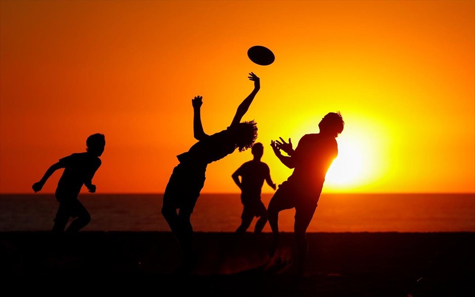 Ειδυλλιακό παιχνίδι. Μια ομάδα αγοριών παίζει μπάλα στην αμμουδιά με φόντο το ηλιοβασίλεμα στην πόλη Ενσινίτας, στην Καλιφόρνια.