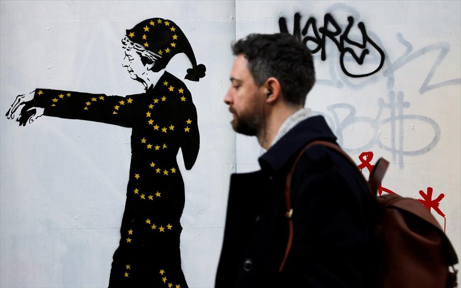 Walking... May. Ένας άνδρας περνάει δίπλα από έναν τοίχο με ένα ειρωνικό γκράφιτι για την Τερέζα Μέι.