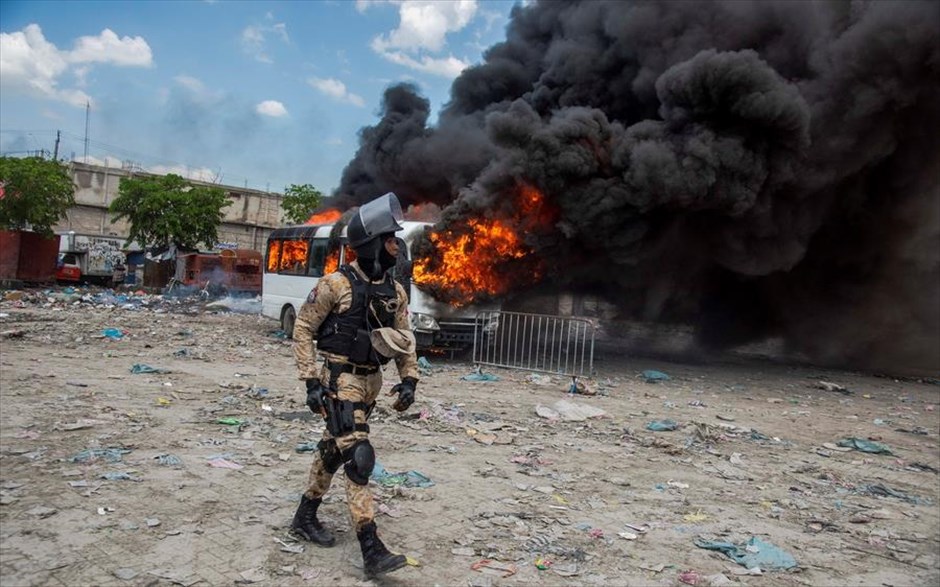Ένταση στην Αϊτή. Αστυνομικός στέκεται μπροστά από φλεγόμενο λεωφορείο κατά τη διάρκεια επεισοδίων στο Πορτ-ο-Πρενς της Αϊτής. 