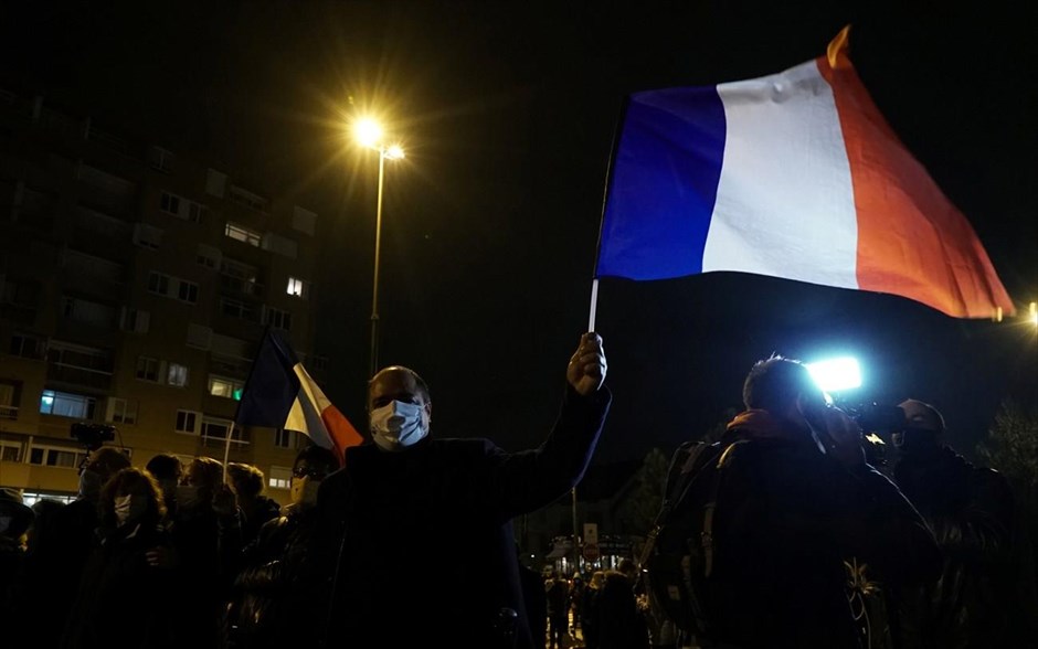 Σιωπηλή πορεία. Άντρας ανεμίζει την Γαλλική σημαία σε πορεία στη μνήμη του αποκεφαλισμένου Γάλλου δασκάλου Σαμιουέλ Πάτι, Γαλλία