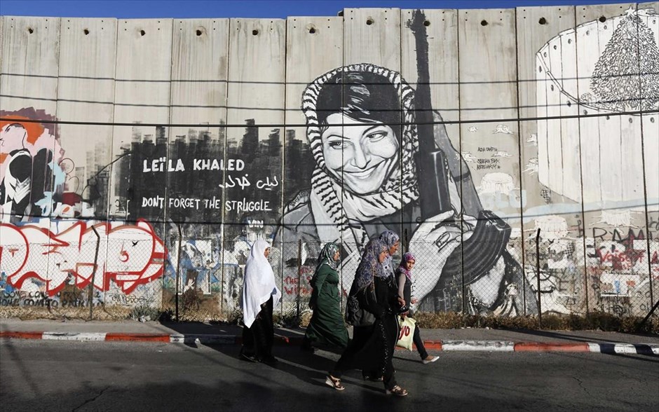 Καθημερινή ζωή στη Δυτική Όχθη. Παλαιστίνιες περνούν μπροστά από ένα γκράφιτι ζωγραφισμένο πάνω στο τείχος του Ισραήλ στη Δυτική Όχθη, ενώ κατευθύνονται προς ένα ισραηλινό σημείο ελέγχου στην πόλη της Βηθλεέμ.