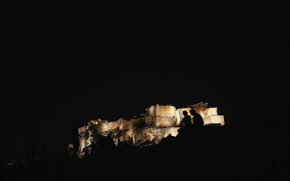 Με θέα την Ακρόπολη. Τουρίστες στο λόφο του Αρεοπαγίτου ατενίζουν τη θέα του φωτισμένου βράχου της Ακρόπολης.
