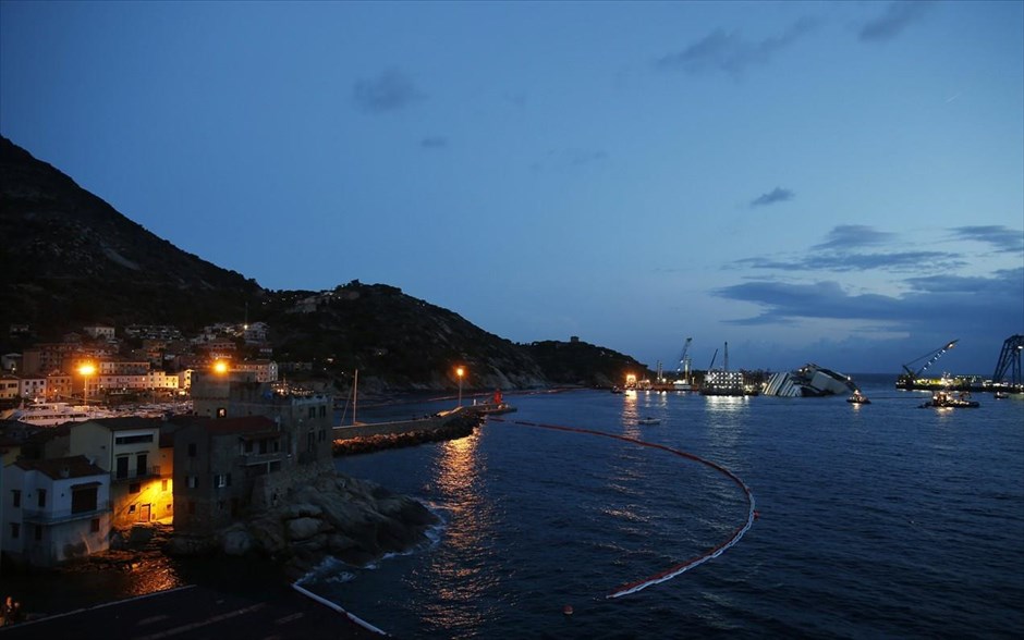 Επιχείρηση ανέλκυσης του Costa Concordia 1. Το ναυαγισμένο κρουαζιερόπλοιο Costa Concordia, βυθισμένο από τη δεξιά του πλευρά κοντά στα βράχια του νησιού Τζίλιο.