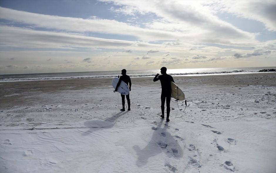 ΗΠΑ - κακοκαιρία - χιόνι. Σέρφερς κοιτάζουν τη θάλασσα στην καλυμμένη από χιόνι παραλία Ροκαγουέι.
