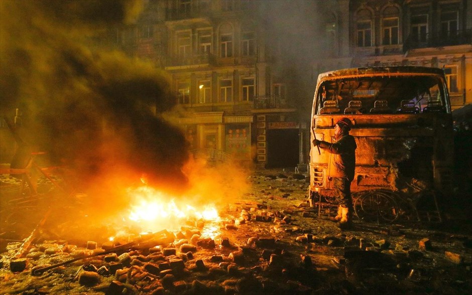 Ουκρανία - Κίεβο - Διαδηλώσεις. Διαδηλωτής στέκεται δίπλα από καμένο όχημα της αστυνομίας.&nbsp;