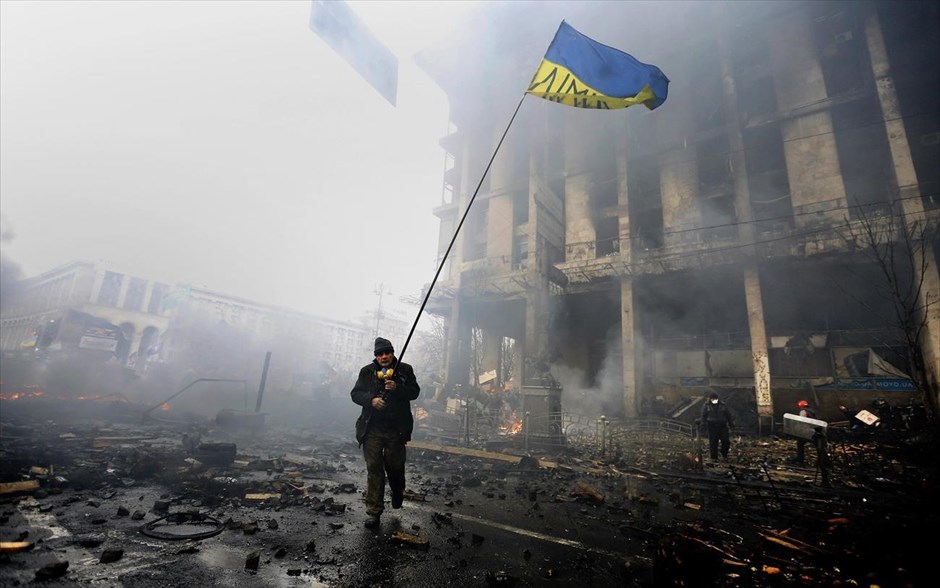 Ουκρανία - Συγκρούσεις στο Κίεβο. Αντικυβερνητικός διαδηλωτής περπατά πλάι στα φλεγόμενα οδοφράγματα κρατώντας στα χέρια του την ουκρανική σημαία.