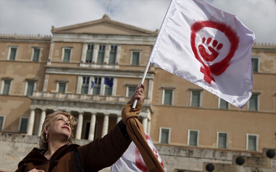 Ημέρα της Γυναίκας - Γυναίκες από όλο τον κόσμο - Ελλάδα. Μία γυναίκα κρατά μία σημαία που απεικονίζει ένα σύμβολο του φεμινισμού κατά τη διάρκεια πορείας για τον εορτασμό της Παγκόσμιας Ημέρας της Γυναίκας.