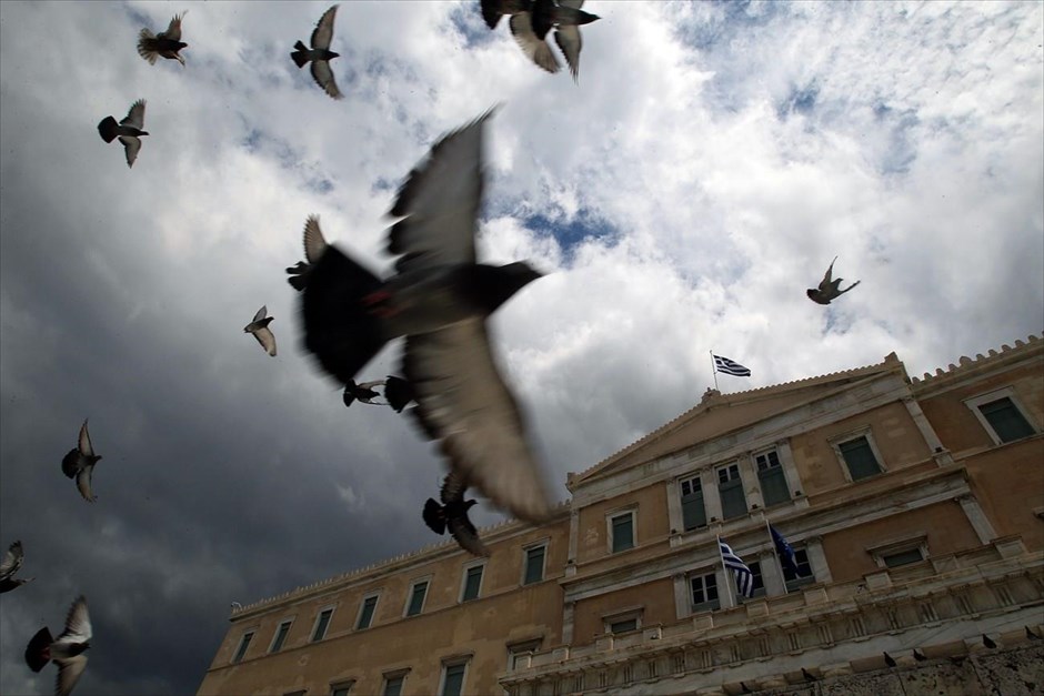 Συννεφιασμένο απόγευμα στην Αθήνα. Περιστέρια πετούν στον συννεφιασμένο ουρανό, δίπλα στο κτήριο της Βουλής.
