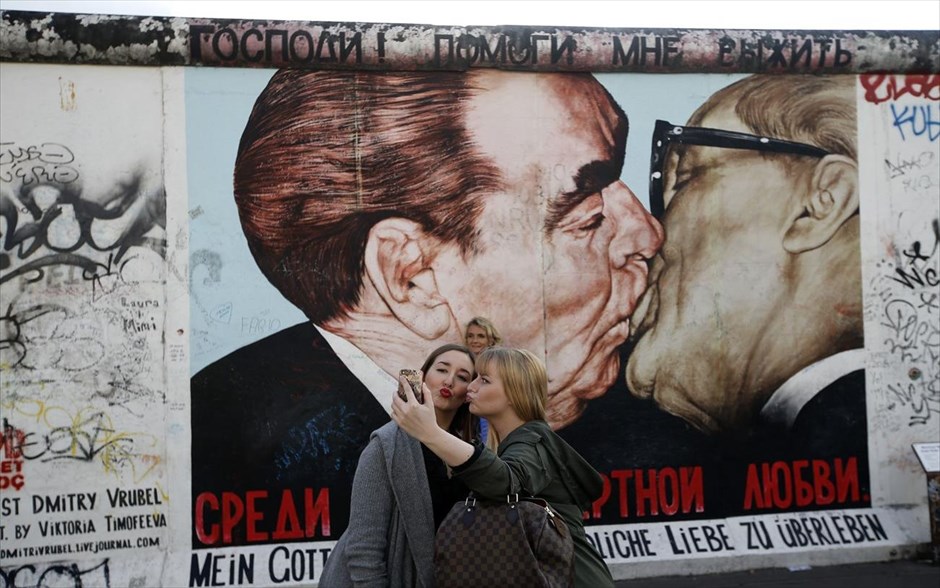 «Selfie» με ένα ιστορικό φιλί. Τουρίστες βγάζουν φωτογραφίες με το κινητό τους τηλέφωνο μπροστά από μία τοιχογραφία που απεικονίζει το ιστορικό φιλί μεταξύ του Γενικού Γραμματέα του Κομμουνιστικού Κόμματος της ΕΣΣΔ Λεονίντ Μπρέζνιεφ και του ομολόγου του Έριχ Χόνεκερ (δεξιά) από τη Λαϊκή Δημοκρατία της Γερμανίας, τον Ιούνιο του 1979, η οποία βρίσκεται στην Ανοιχτή Πινακοθήκη της ανατολικής πλευράς (East Side Gallery). Η Γερμανία θα γιορτάσει την 25η επέτειο από την πτώση του τείχους του Βερολίνου στις 9 Νοεμβρίου.