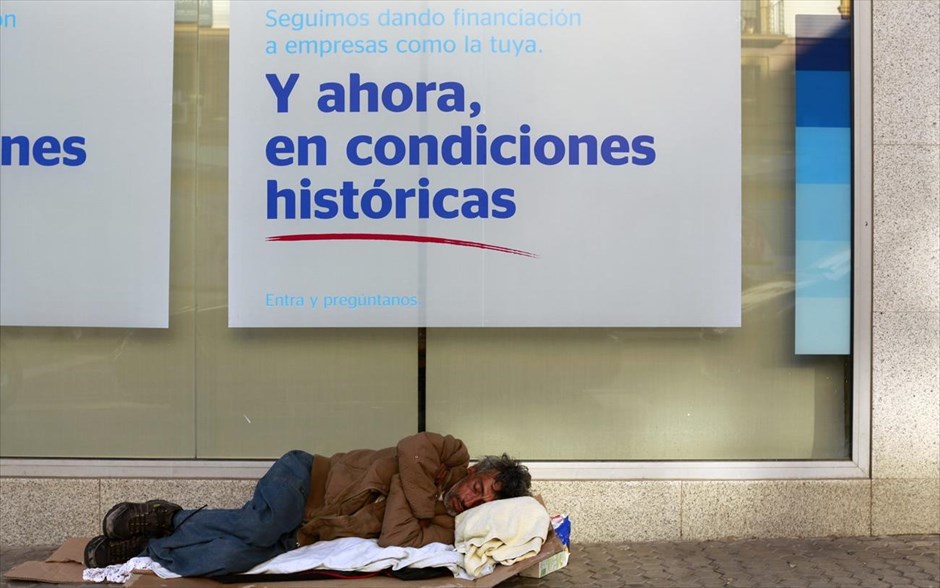 Αστεγος στη Σεβίλλη . Άστεγος άνδρας κοιμάται σε πεζοδρόμιο έξω από ένα υποκατάστημα της τράπεζας BBVA στην πρωτεύουσα της Ανδαλουσίας, Σεβίλλη. Στη διαφημιστική πινακίδα της τράπεζας αναγράφεται: «Συνεχίζουμε να παρέχουμε χρηματοδότηση σε εταιρείες σαν τη δική σας. Και τώρα, με ιστορικούς όρους. Ελάτε να μας ρωτήσετε».