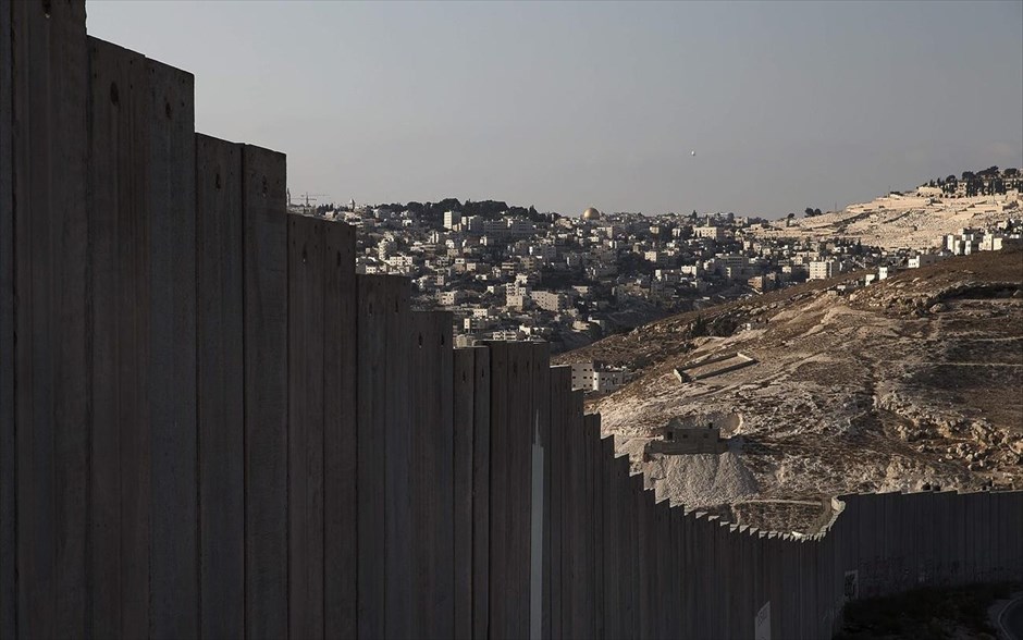 Τα τείχη που χωρίζουν τον κόσμο - Δυτική Όχθη. Ο Θόλος του Βράχου στην παλιά πόλη της Ιερουσαλήμ διακρίνεται στο βάθος, πίσω από τμήμα του τείχους που χωρίζει το Ισραήλ από τη Δυτική Όχθη, στην πόλη Άμπου Ντις. Το τείχος που χωρίζει το Ισραήλ από τη Δυτική Όχθη αποτελείται από φράχτες, αγκαθωτό συρματόπλεγμα και πλάκες τσιμέντου. Η ισραηλινή κυβέρνηση ενέκρινε την ανέγερσή του τείχους το 2002 και σύμφωνα με τα Ηνωμένα Έθνη έχει ολοκληρωθεί σχεδόν το 60% του αρχικού σχεδιασμού. Το Διεθνές Δικαστήριο της Χάγης το έκρινε παράνομο το 2004, όμως το Ισραήλ το διατηρεί και το ενισχύει με το επιχείρημα ότι αποτελεί προστασία από τις επιθέσεις των Παλαιστινίων.