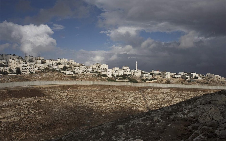 Τα τείχη που χωρίζουν τον κόσμο - Δυτική Όχθη. Προσφυγικός καταυλισμός στην Σουαφάτ, στη Δυτική Όχθη, διακρίνεται πάνω από το τμήμα του αμφιλεγόμενου τείχους του Ισραήλ. Το τείχος που χωρίζει το Ισραήλ από τη Δυτική Όχθη αποτελείται από φράχτες, αγκαθωτό συρματόπλεγμα και πλάκες τσιμέντου. Η ισραηλινή κυβέρνηση ενέκρινε την ανέγερσή του τείχους το 2002 και σύμφωνα με τα Ηνωμένα Έθνη έχει ολοκληρωθεί σχεδόν το 60% του αρχικού σχεδιασμού. Το Διεθνές Δικαστήριο της Χάγης το έκρινε παράνομο το 2004, όμως το Ισραήλ το διατηρεί και το ενισχύει με το επιχείρημα ότι αποτελεί προστασία από τις επιθέσεις των Παλαιστινίων.