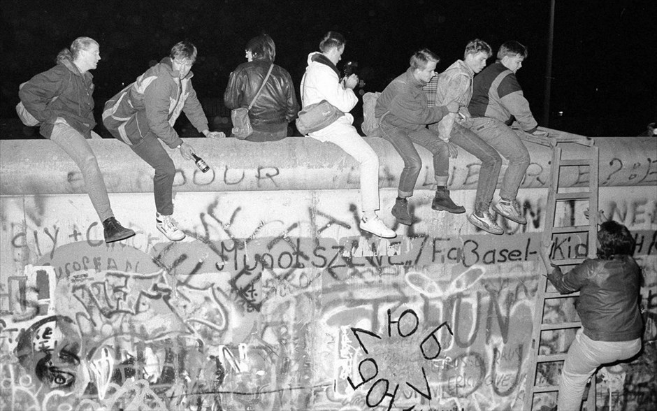 Η πτώση του Τείχους του Βερολίνου. Πολίτες της Δυτικής Γερμανίας κάθονται πάνω στο Τείχος του Βερολίνου κοντά στο σημείο ελέγχου Τσάρλι, μετά την ανακοίνωση για το άνοιγμα των συνόρων της Ανατολικής Γερμανίας στο Βερολίνο (φωτογραφία αρχείου, 9 Νοεμβρίου 1989).