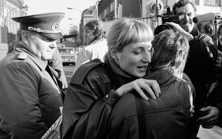 Η πτώση του Τείχους του Βερολίνου. Μία γυναίκα από το Δυτικό Βερολίνο αγκαλιάζει ένα πολίτη από την Ανατολική πλευρά, στο σημείο ελέγχου Invalidenstrasse, μετά την ανακοίνωση για το άνοιγμα των συνόρων της Ανατολικής Γερμανίας στο Βερολίνο (φωτογραφία αρχείου, 10 Νοεμβρίου 1989).
