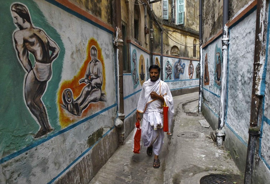 Καθημερινή ζωή στην Ινδία. Ινδουιστής ιερέας περπατά σε σοκάκι, με τοιχογραφίες που απεικονίζουν σκηνές από προπόνηση πάλης, στην Καλκούτα της Ινδίας. 