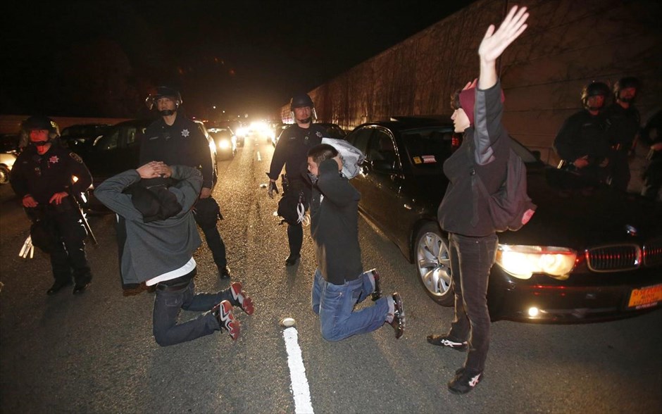Φέργκιουσον - Επεισόδια μετά την απόφαση για τον αστυνομικό - Καλιφόρνια. Διαδηλωτές έχουν γονατίσει σηκώνοντας τα χέρια τους ψηλά μπροστά από αστυνομικούς, στον αυτοκινητόδρομο 580, στο Όκλαντ της Καλιφόρνια, κατά τη διάρκεια διαδήλωσης μετά την ανακοίνωση της απόφασης του σώματος των ενόρκων να μην παραπεμφθεί σε δίκη ο αστυνομικός Ντάρεν Ουίλσον, που στις 9 Αυγούστου σκότωσε τον άοπλο 18χρονο Αφροαμερικανό Μάικλ Μπράουν.