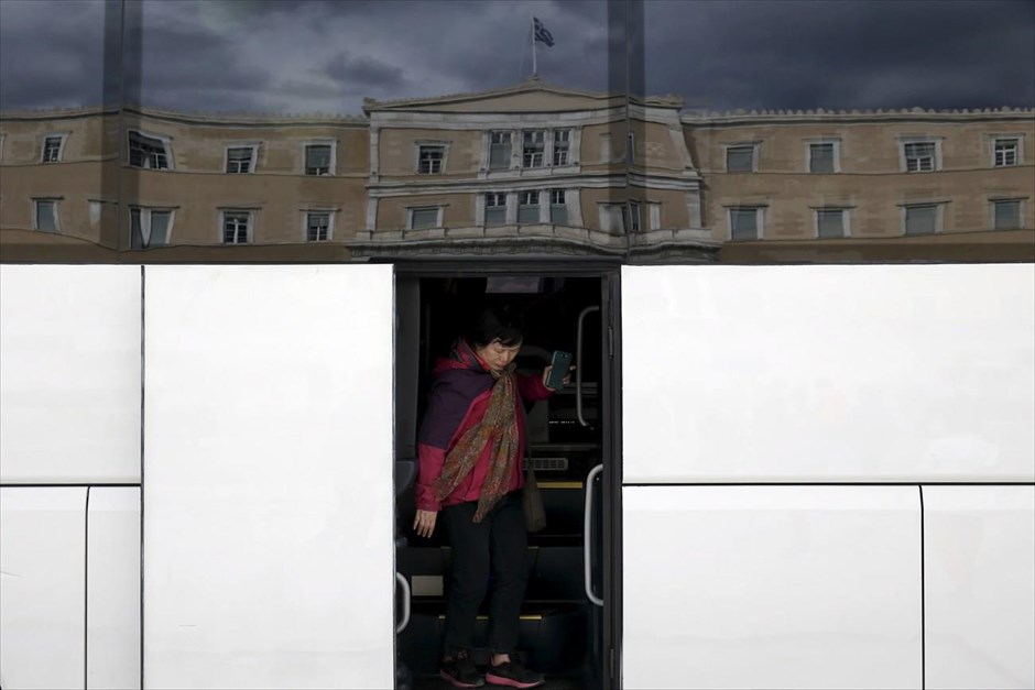 Στιγμιότυπο από το κέντρο της Αθήνας. Μια γυναίκα αποβιβάζεται από τουριστικό λεωφορείο, στα παράθυρα του οποίου αντικατοπτρίζεται το κτήριο της Βουλής. &nbsp;