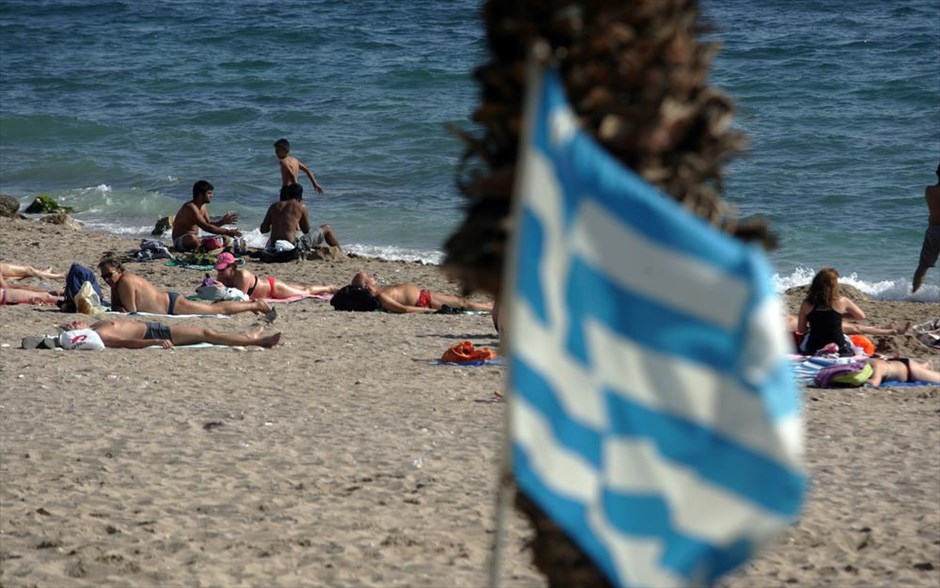 Ανάσα δροσιάς στις παραλίες της Αττικής. Μία ελληνική σημαία ανεμίζει, ενώ κόσμος κάνει μπάνιο στην παραλία του Φλοίσβου.