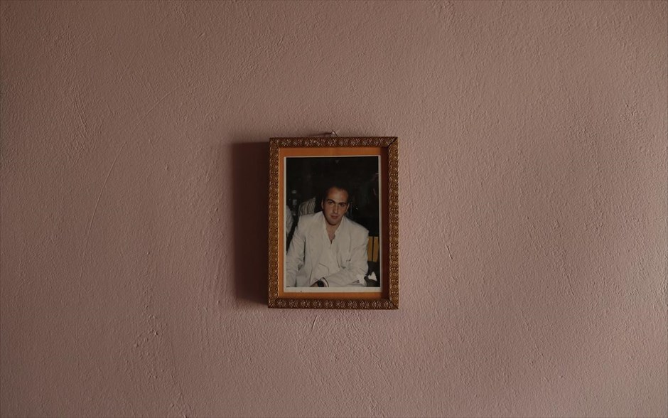 «Όταν ζούσε η μητέρα μου» 8. Στη φωτογραφία, μια κορνίζα με τη φωτογραφία του Ιάκωβου, άνεργου 41 χρονών, στο εξοχικό του στο Πόρτο Ράφτη. Ο Ιάκωβος για να μπορέσει να πληρώσει τα χρέη του στην εφορία αναγκάζεται να πουλήσει σε εξαιρετικά χαμηλή τιμή το εξοχικό του σπίτι όπου είχε περάσει μαζί με τους γονείς του όλα τα καλοκαίρια της ζωής του.