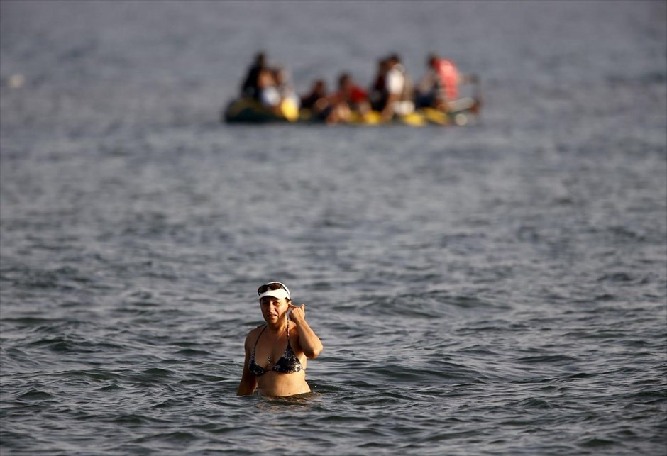 Προσφυγικό - Μετανάστες - Πρόσφυγες - Κως. Μια γυναίκα κάνει μπάνιο σε παραλία της Κω, ενώ πίσω της διακρίνεται σκάφος που μεταφέρει πρόσφυγες. 